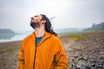 Long haired man standing in a rain soaked landscape shaking his head and smiling 