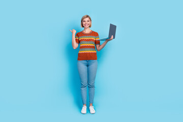 Full size photo of cheerful woman dressed knit t-shirt hold laptop indicating at sale empty space isolated on blue color background