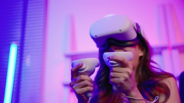 Female gamer with VR glasses girl having fun playing games in a room filled with neon lights.
