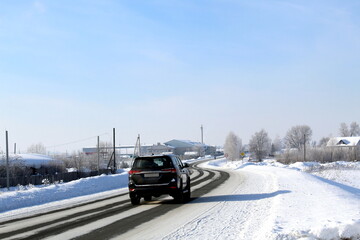 A black car is driving along a winter highway.