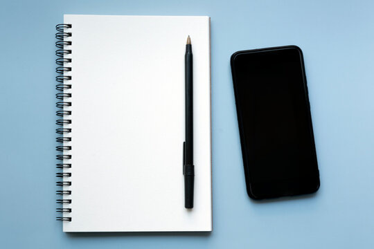 Smartphone with notebook and pen on blue background. Copy space.
