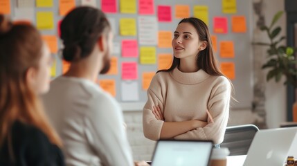 A young professional woman engages in a collaborative discussion with colleagues amidst colorful sticky notes in a bright office setting.
