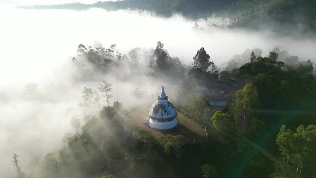 An old white buddhist temple stupa in the morning shine of sunbeams and clouds in the mountains and tropical jungle forest of Sri Lanka