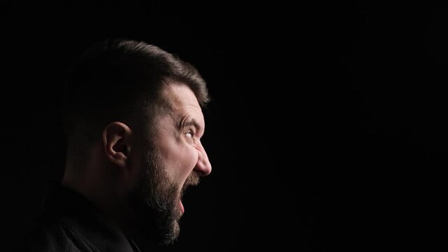Close up profile portrait of a aggressive screaming Caucasian man on black background. Rage, frustration, negative emotions concept.