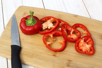 On a wooden table lies a cutting board with chopped red bell peppers and a knife.