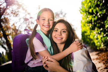 Portrait of two peaceful adorable girls beaming smile cuddle enjoy warn sunny weather after school...