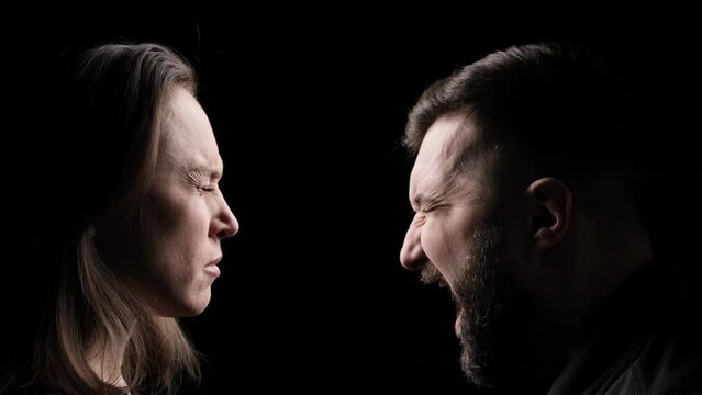 Portrait of a aggressive Caucasian man shouts at a woman on a black background. Family conflicts, domestic violence, wife and husband confrontation concept.
