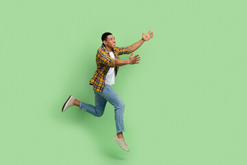 Fototapeta na wymiar Full body profile portrait of carefree young man jump run arms catch empty space isolated on green color background