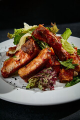 Close-up of BBQ ribs with mixed salad on a white plate