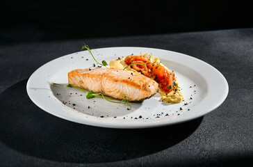 Salmon steak with hummus and tomatoes on a white plate