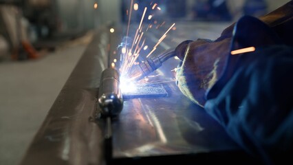 Close-up of a welder welding metal. A welder in a mask welds metal and sparks the metal. Welding...