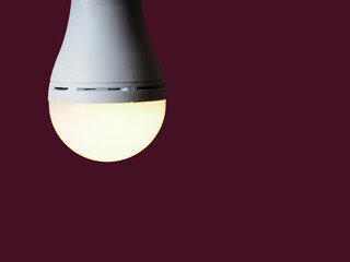 A switched-on LED rechargeable lamp in the hands of a person on a burgundy background