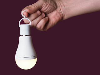 A switched-on LED rechargeable lamp in the hands of a person on a burgundy background
