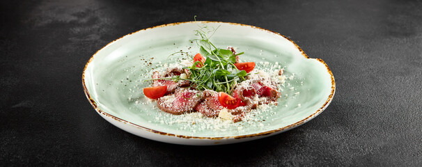 Roast beef carpaccio with Parmesan, arugula, and tomatoes on a speckled turquoise plate