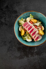Top view of a Nicoise salad featuring medium-rare sliced tuna, potatoes, eggs, and greens in a rustic teal bowl