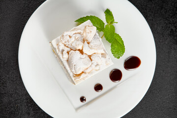 Delicate meringue cake with creamy cheese filling, garnished with a sprig of mint on a white plate