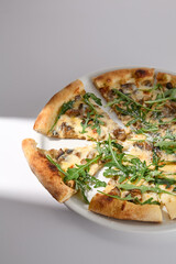 Savory Italian pizza with cheese and mushrooms, highlighted with fresh arugula, cast in soft shadow on a white plate