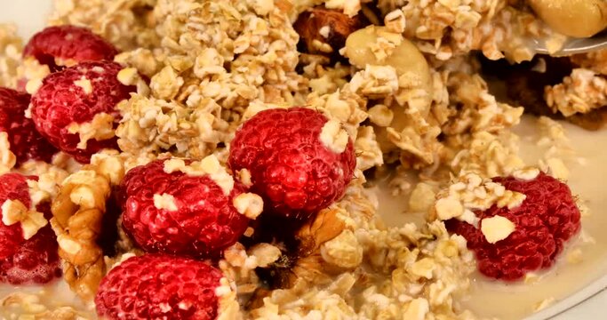 Close up video of a natural, healthy and very delicious muesli mixed by a spoon with oat milk and raspberries