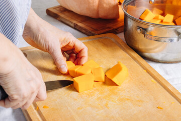 Woman's hands cut pumpkin into slices on a wooden board, side view. The food preparation process