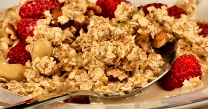 Macro video of a natural, healthy and very delicious muesli with nuts and red raspberries. Oat milk is mixed in with a spoon