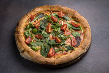 Pizza with salami, arugula and cherry tomatoes on black background
