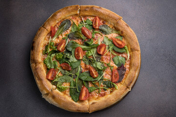 Pizza with salami, arugula and cherry tomatoes on black background