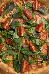 Pizza with salami, arugula and cherry tomatoes on black background