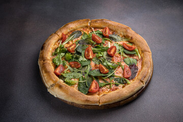 Pizza with salami, arugula and cherry tomatoes on black background