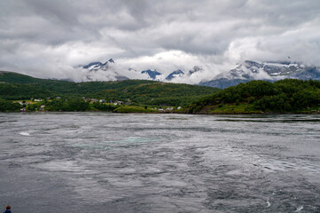 Panorama of snowy mountains in the clouds and water level of the sea in the fjord. Sea eddies on the water - Saltstraumen, Norway
