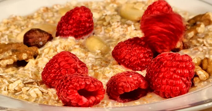 Raspberries drop into a bowl of spelled muesli. Spelled is rich in magnesium, iron, zinc and manganese