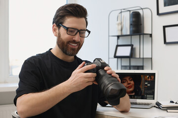 Professional photographer in glasses holding digital camera at table in office