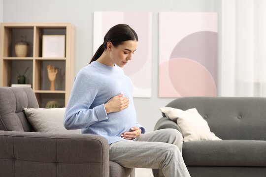 Pregnant young woman on armchair at home, space for text