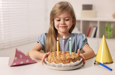 Cute girl with birthday cake at table indoors