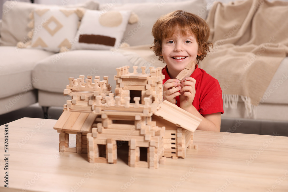 Wall mural Cute little boy playing with wooden castle at table in room. Child's toy