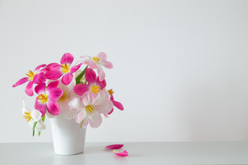 white and pink  tulips in white vase on background wall