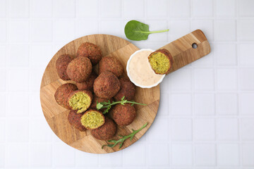 Delicious falafel balls, herbs and sauce on white tiled table, top view