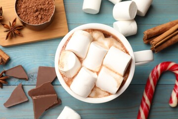 Tasty hot chocolate with marshmallows and ingredients on light blue wooden table, flat lay