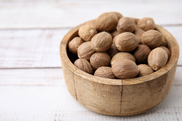 Whole nutmegs in bowl on light wooden table, closeup. Space for text