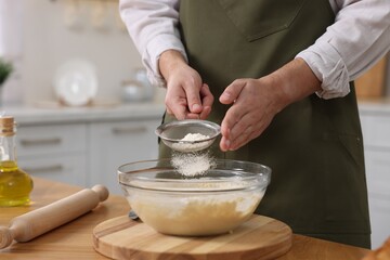Making bread. Man sprinkling flour onto dough at wooden table in kitchen, closeup