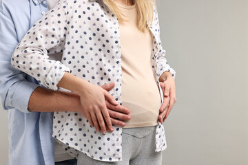 Man touching his pregnant wife's belly on light grey background, closeup. Space for text