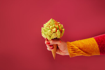 Female hand holding Waffle cone with Romanesco cabbage with dripping fruit sauce as vegetarian...