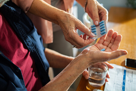 Senior hands dispensing medication from a pill organizer into palm with water glass on table