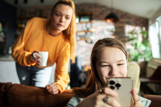 Teen daughter using smartphone with mother in background at home
