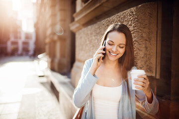 Young adult woman talking on a phone while having a cup of coffee on her commute to work