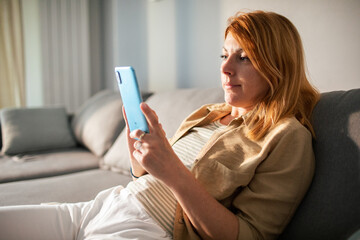 Fototapeta na wymiar Woman smiling while browsing her smartphone at home