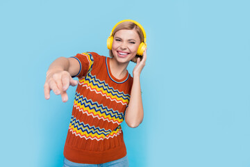 Portrait of satisfied girl with short hairstyle wear knit t-shirt touching headphones enjoy sound isolated on blue color background