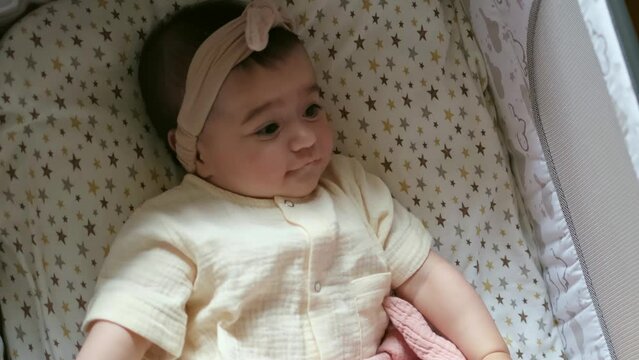 Baby in a cozy bassinet stares pensively, a soft headband framing her thoughtful gaze. The candid moment captures a slice of infant life, pondering the new world.