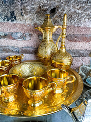 Fototapeta na wymiar Vintage golden tea set with intricate designs on tray against rustic stone wall. Traditional ornate metalware concept for interior design and decoration.