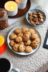 Cup of tea or coffee, stack of books, e-reader, glasses, various cookies, almonds, orange juice and lit candles on the table. Hygge at home. Selective focus.