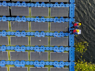 Top aerial of Male workers repair Floating solar panels on water lake. Engineers construct on site Floating solar panels. clean energy for future living. Industrial Renewable energy of green power.